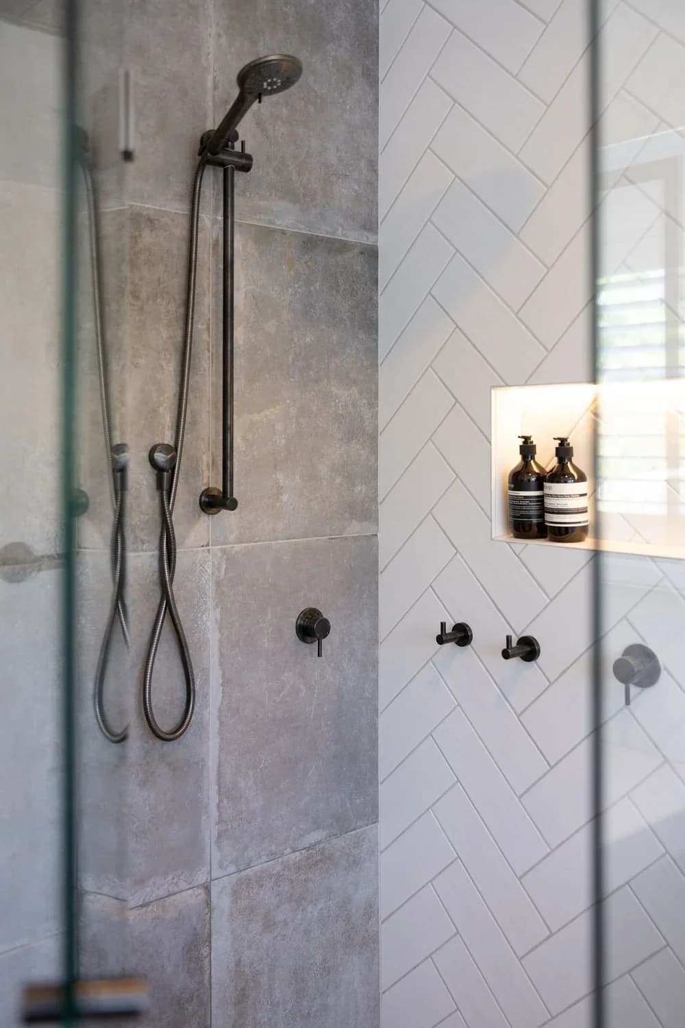 Walk-in shower with gray stone wall, matte black rain showerhead, handheld, herringbone tile, and LED-lit niche — Issaquah WA