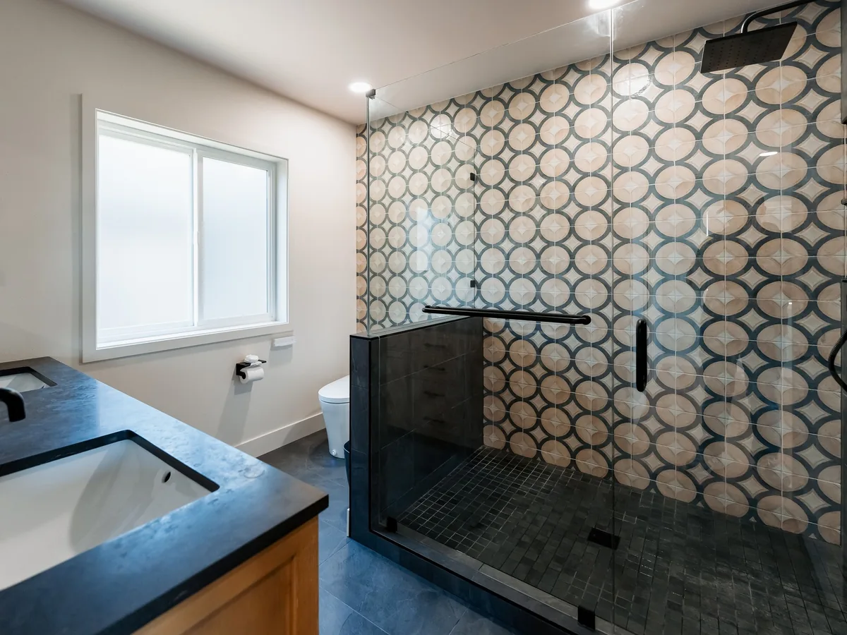 Walk-in shower with a patterned porcelain wall and frameless glass beside a window and a black quartz vanity, Capitol Hill Seattle