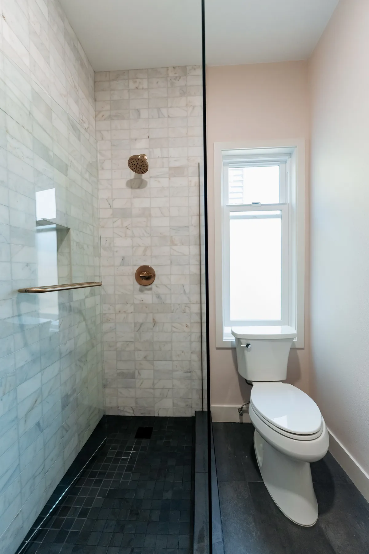 Walk-in shower in marble subway tile with brass fixtures, a black mosaic floor and a window beside it, Capitol Hill Seattle