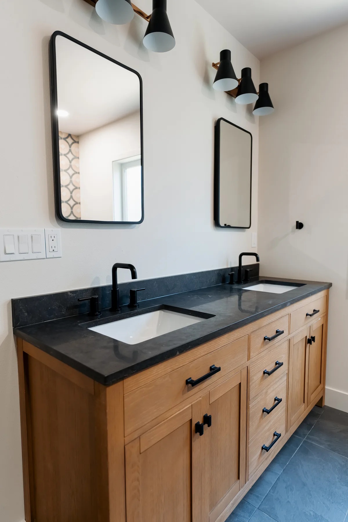 Oak double vanity with black quartz top, two black-framed mirrors and sconces