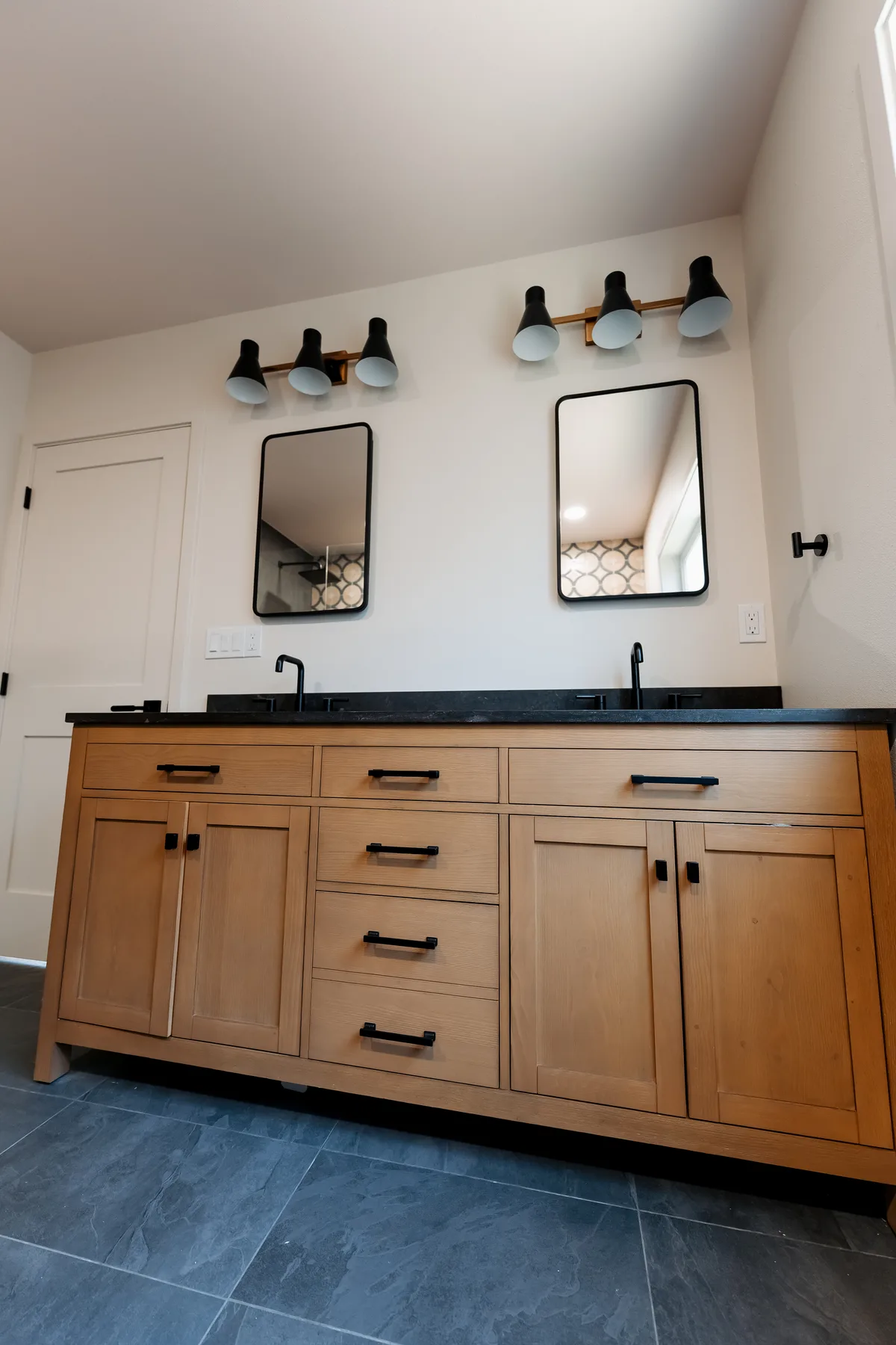 Oak double vanity with black quartz top and two black-framed mirrors