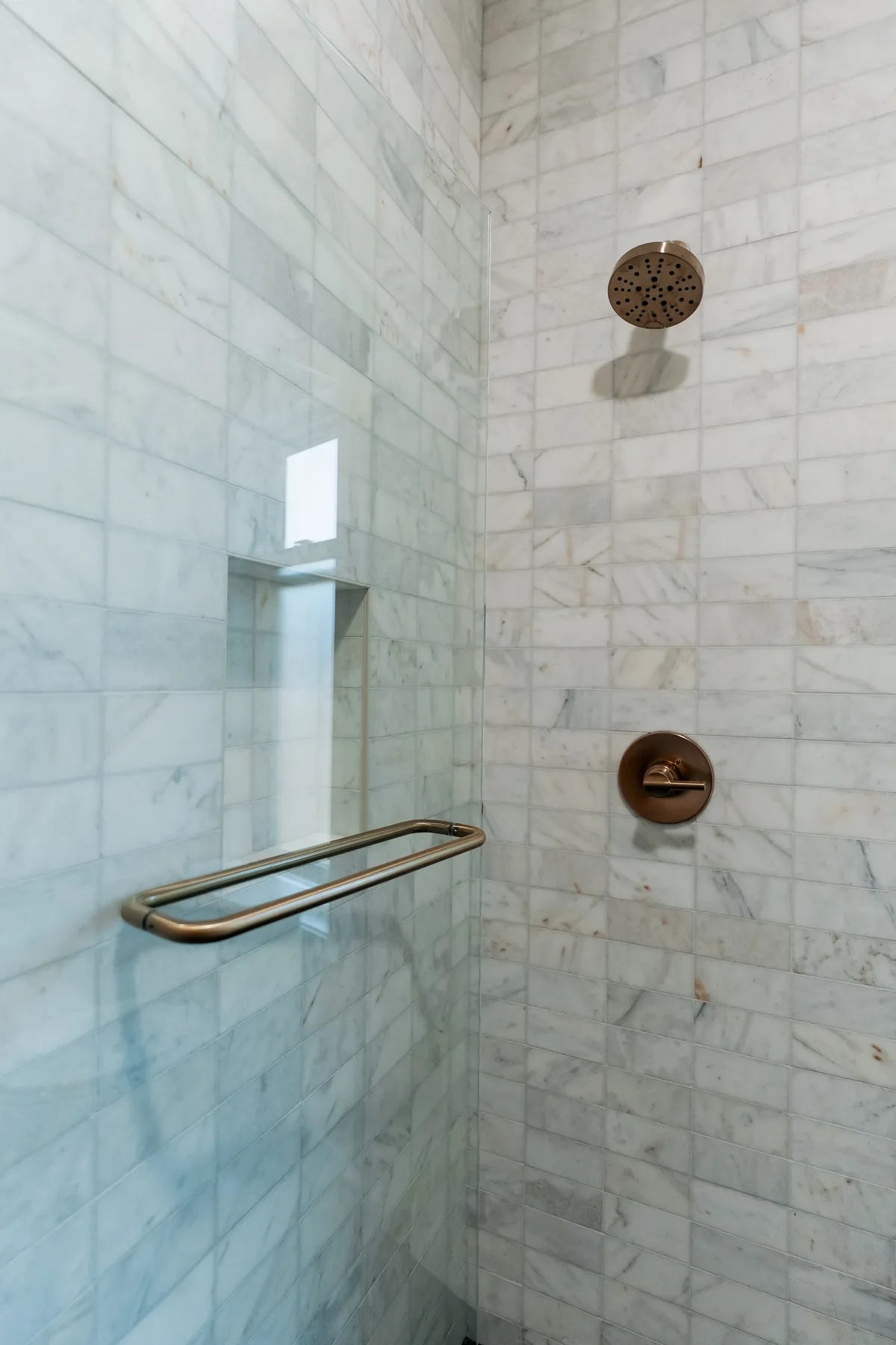 Marble subway shower tile with brass shower head and grab bar
