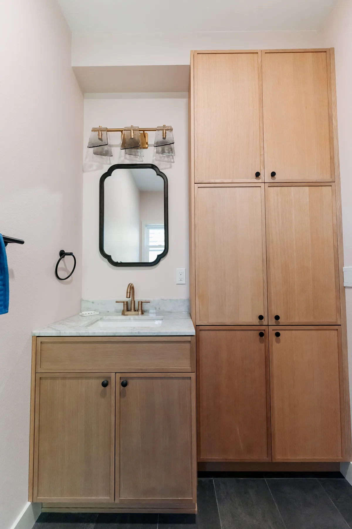 Compact oak vanity with marble top and a tall linen cabinet