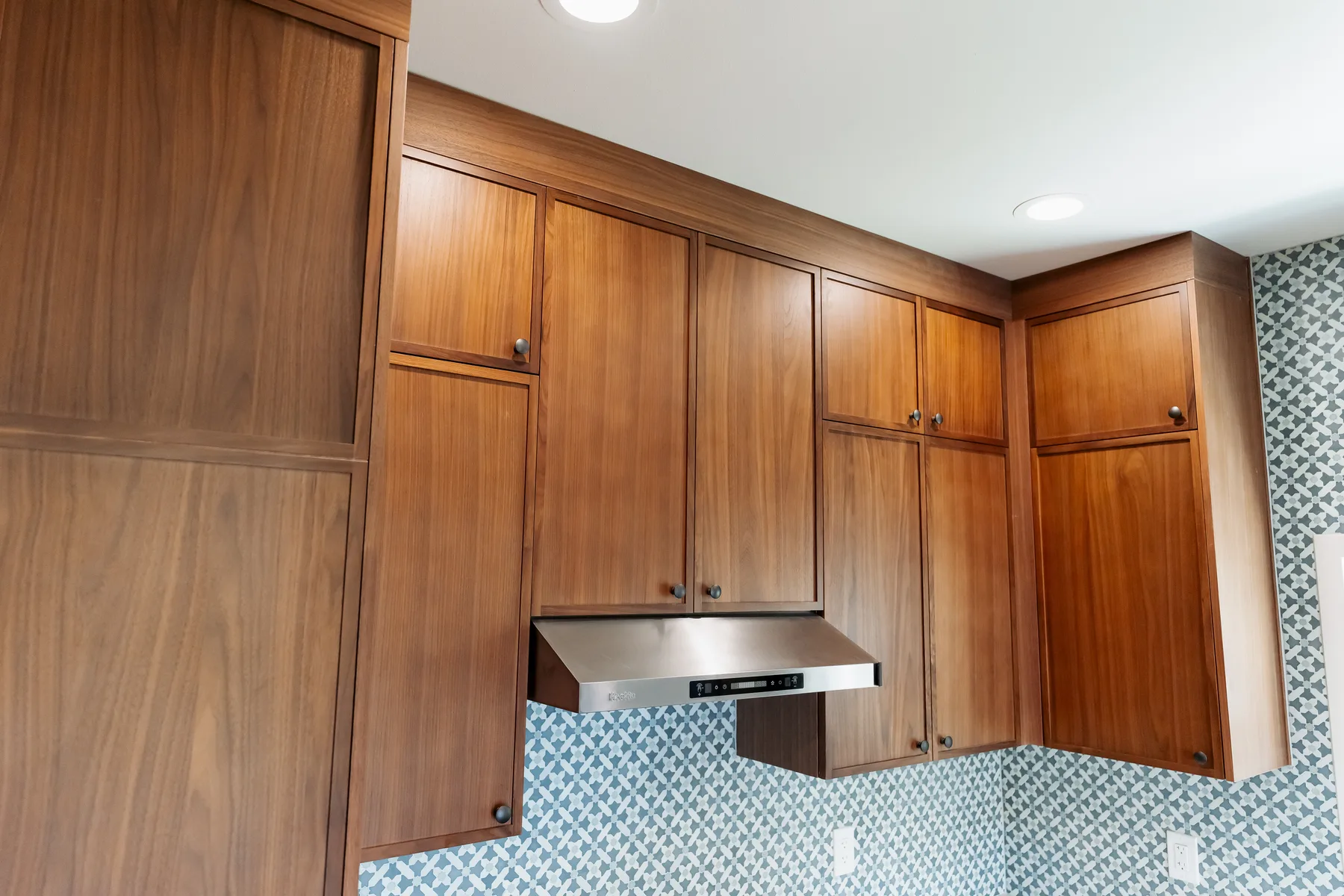 Walnut kitchen cabinets with stainless range hood and blue tile