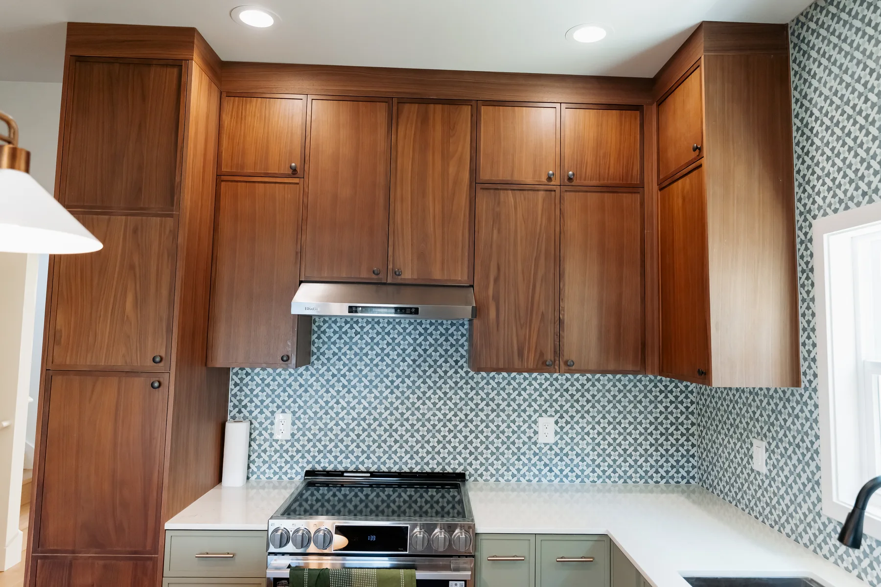 Range wall with walnut upper cabinets, sage lower cabinets and blue penny-round tile