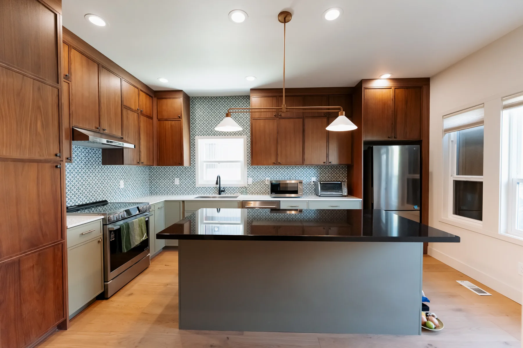 Finished kitchen with walnut cabinets, black quartz island and blue penny-round tile backsplash