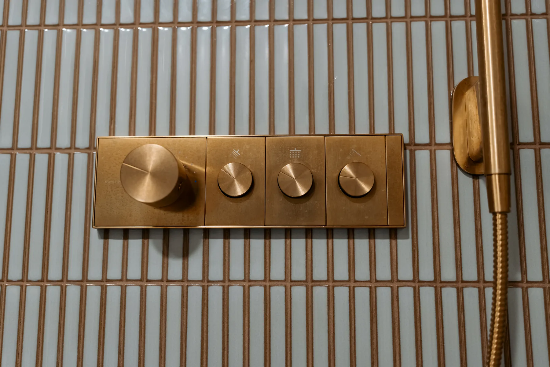 Brass thermostatic shower valve with four controls set in kit-kat tile