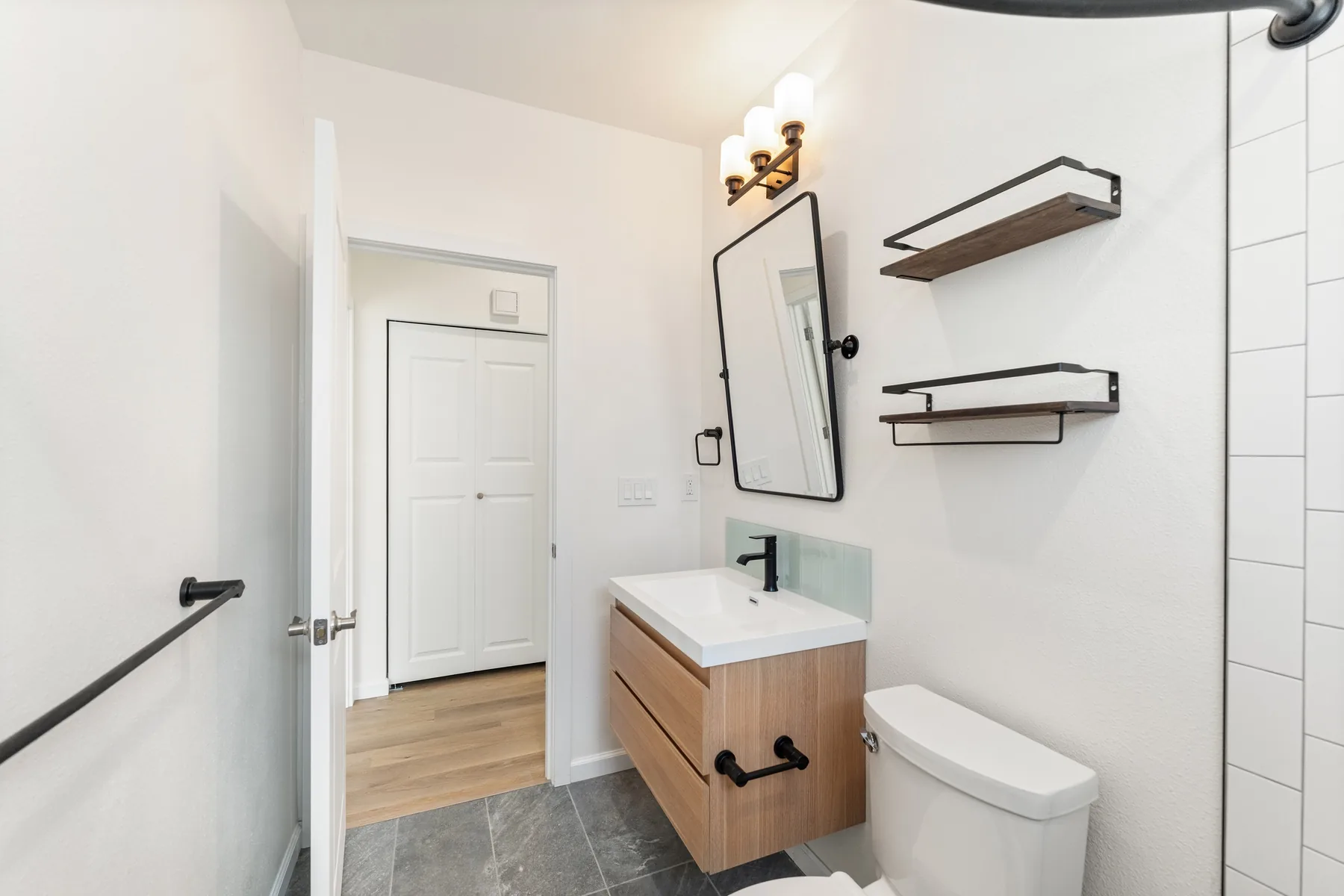 Floating vanity with black-framed mirror and open wood shelves by the door, View Ridge ADU bathroom